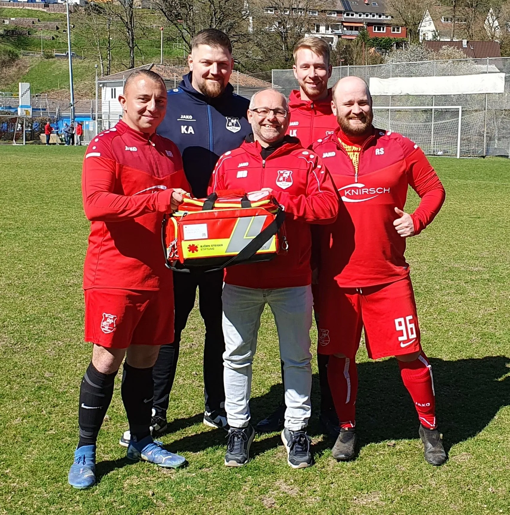 Gruppenfoto Spieler in roter Vereinskleidung Verbandskasten haltend