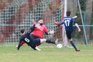 Fußballspieler schießt ein Tor vor Torwart und Gegenspieler